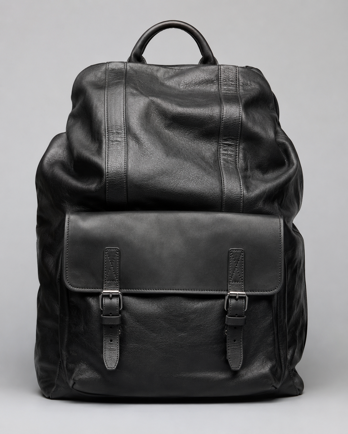 Premium black leather backpack with front flap pocket, buckle straps, and soft genuine leather texture on a light grey studio background.